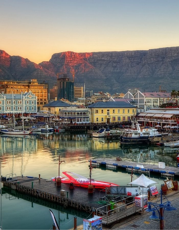 Visitors enjoying the vibrant Cape Town Waterfront with views of boats, shops, and mountains, guided by Extraordinary Tours